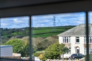 A rural landscape with a house, a car, and a wind turbine in the distance. - Modern Studio Near Port Isaac (Bodmin)