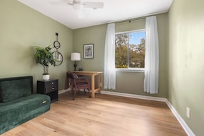 A room with a green wall, a wooden desk, a chair, a sofa, a potted plant, a ceiling fan, and a window with white curtains. - 4 Bdrm, Spacious, Pool, Patio, Yard Games (Austin)