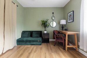 A room with a green sofa, a wooden desk, a chair, a potted plant, a mirror, and a framed picture on the wall. - 4 Bdrm, Spacious, Pool, Patio, Yard Games (Austin)