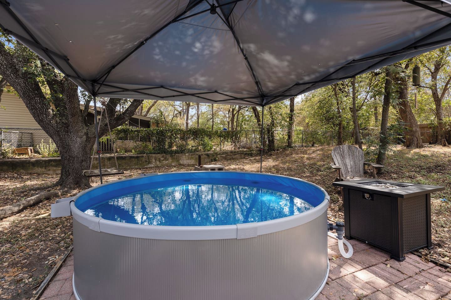 An outdoor hot tub under a canopy, surrounded by trees and a patio area.