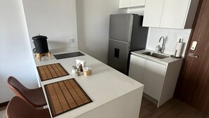 Eine moderne Küche mit weißen Schränken, einem Edelstahlkühlschrank, einer kleinen Kochinsel mit Hockern und Holzboden.