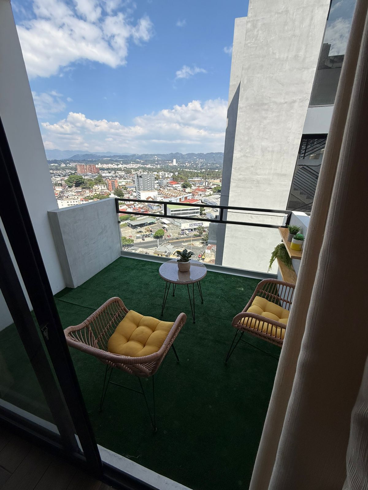 A balcony with two wicker chairs, a small round table, and a view of a cityscape.