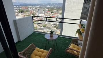 A balcony with two wicker chairs, a small round table, and a view of a cityscape.