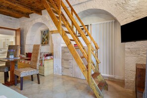 Ein Zimmer mit einer Holztreppe, einer Essecke mit Korbmöbeln und einer Heizkörper.