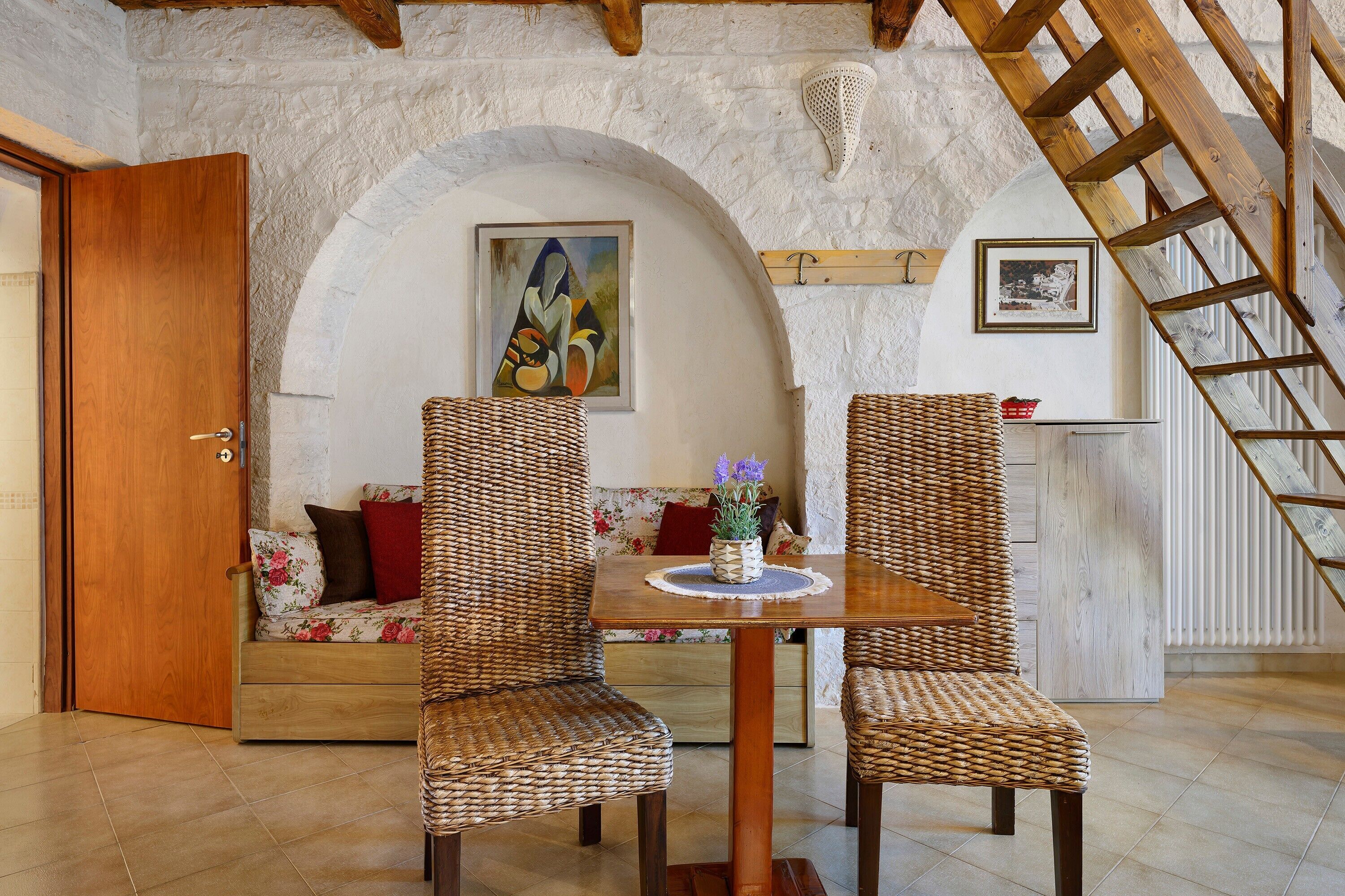 A cozy room with a wooden table and chairs, a sofa with floral cushions, and a painting on the wall.