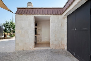 A building with a concrete exterior, a dark garage door, and a small doorway leading to an interior space. - Room 'Camera Primo Piano' with Shared Pool, Wi-Fi and Air Conditioning (Martina Franca)