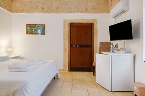A hotel room with a bed, a wooden door, a television, a refrigerator, and a painting on the wall. - Room 'Camera Primo Piano' with Shared Pool, Wi-Fi and Air Conditioning (Martina Franca)