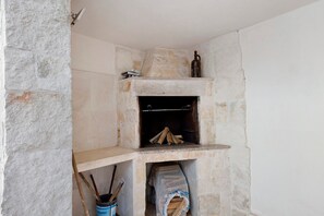 Ein Kamin aus Stein mit einer Ablage darüber, einem hängenden Topf und einem Holzkorb darunter.