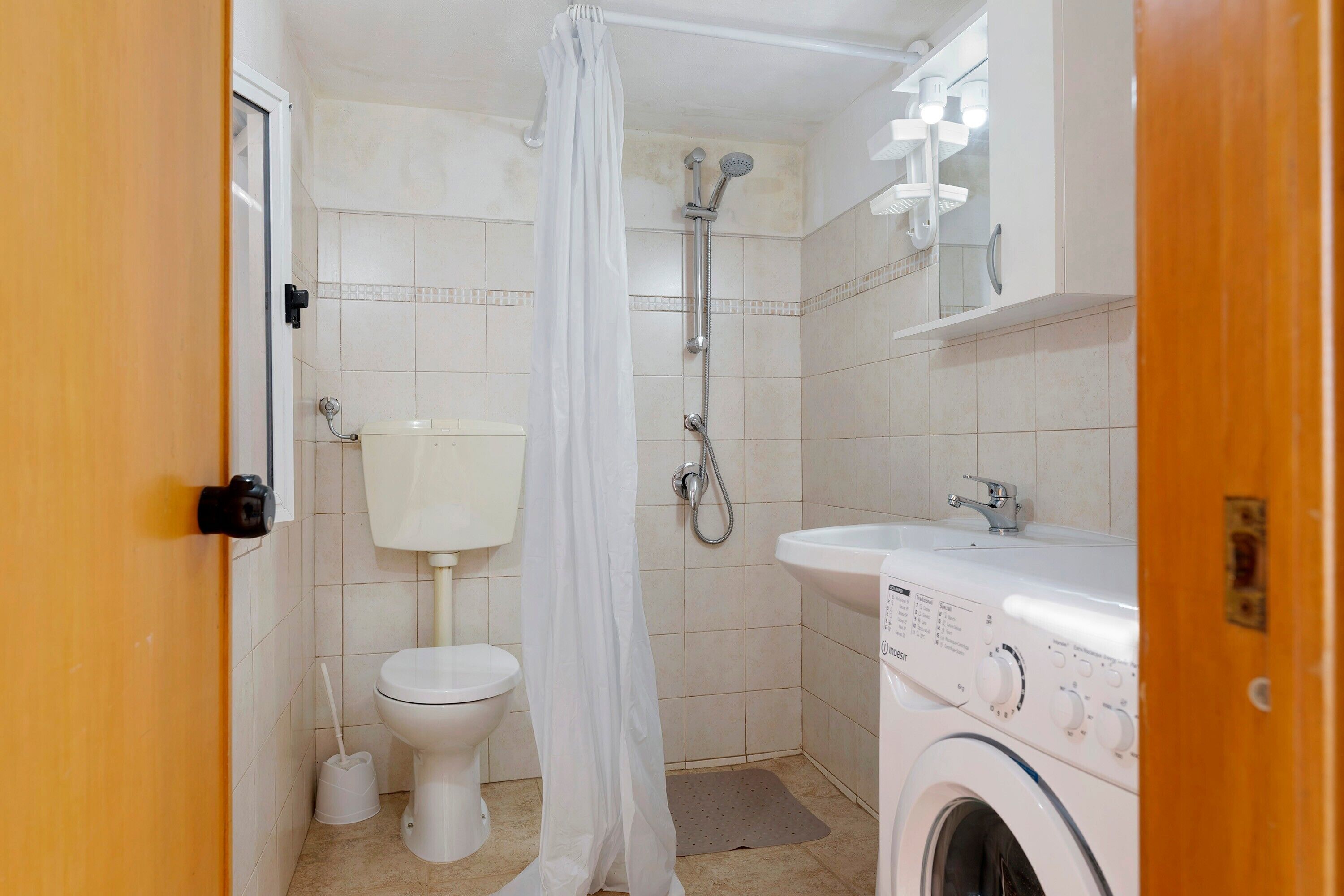 A small, compact bathroom with a toilet, shower, and washing machine.