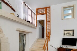 Eine Treppe führt zu einer oberen Etage, mit einem Holnlaufgeländer, einem Fernseher auf einer Holzkommode und einem gerahmten Bild an der Wand.
