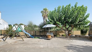 Ein Spielplatz mit Rutsche, Schaukeln, einem Baum und einem Picknicktisch mit Sonnenschirm.