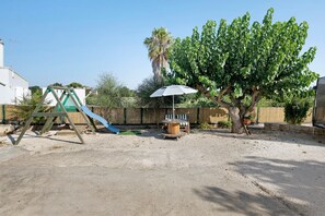 Ein Spielplatz mit Rutsche, Schaukeln, einem Baum und einem Picknicktisch mit Sonnenschirm.