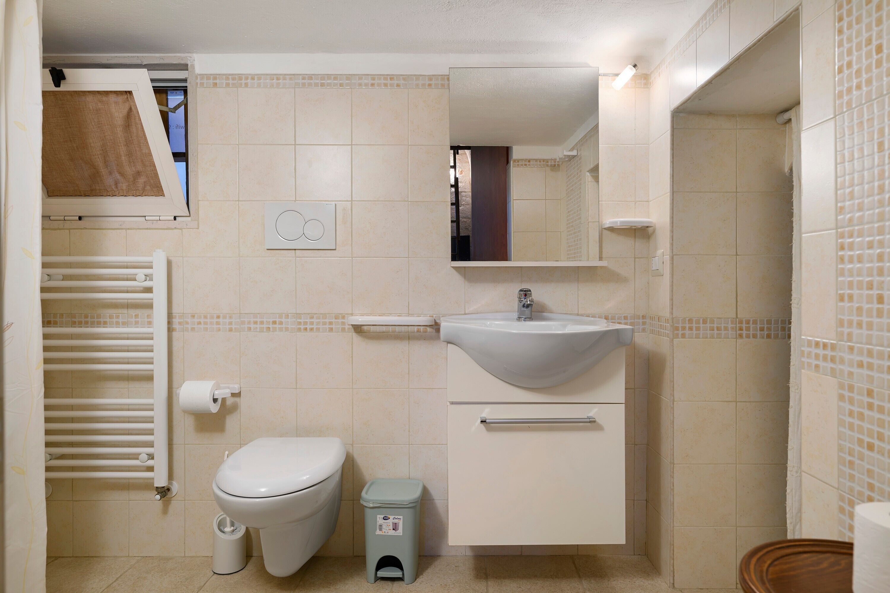 A bathroom with a toilet, sink, mirror, towel rack, and a small trash bin.