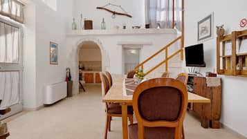 Een eetruimte met een houten tafel en stoelen, een trap en een televisie op een houten dressoir.