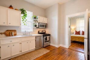 A modern kitchen with white cabinetry, a microwave, stove, and a sink. There is a wooden cutting board and salt and pepper shakers on the counter. A plant is visible through the window blinds. - 2-Home Austin Compound | Hot Tub + Cowboy Pool (Austin)