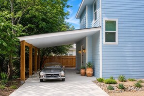 A house with a covered driveway, a parked car, and a wooden fence. - 2-Home Austin Compound | Hot Tub + Cowboy Pool (Austin)