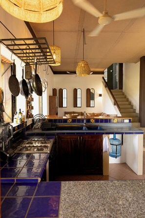 Une cuisine équipée d’une cuisinière à gaz, de casseroles suspendues et d’un plan de travail bleu recouvert de carreaux.