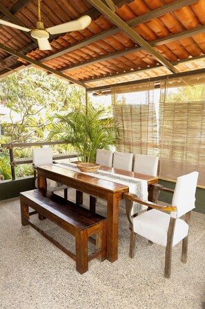 A wooden table with benches and chairs, a ceiling fan, and a view of greenery outside. - Beautiful home in La Punta with a private pool, rooftop terrace, and AC. (Puerto Escondido)