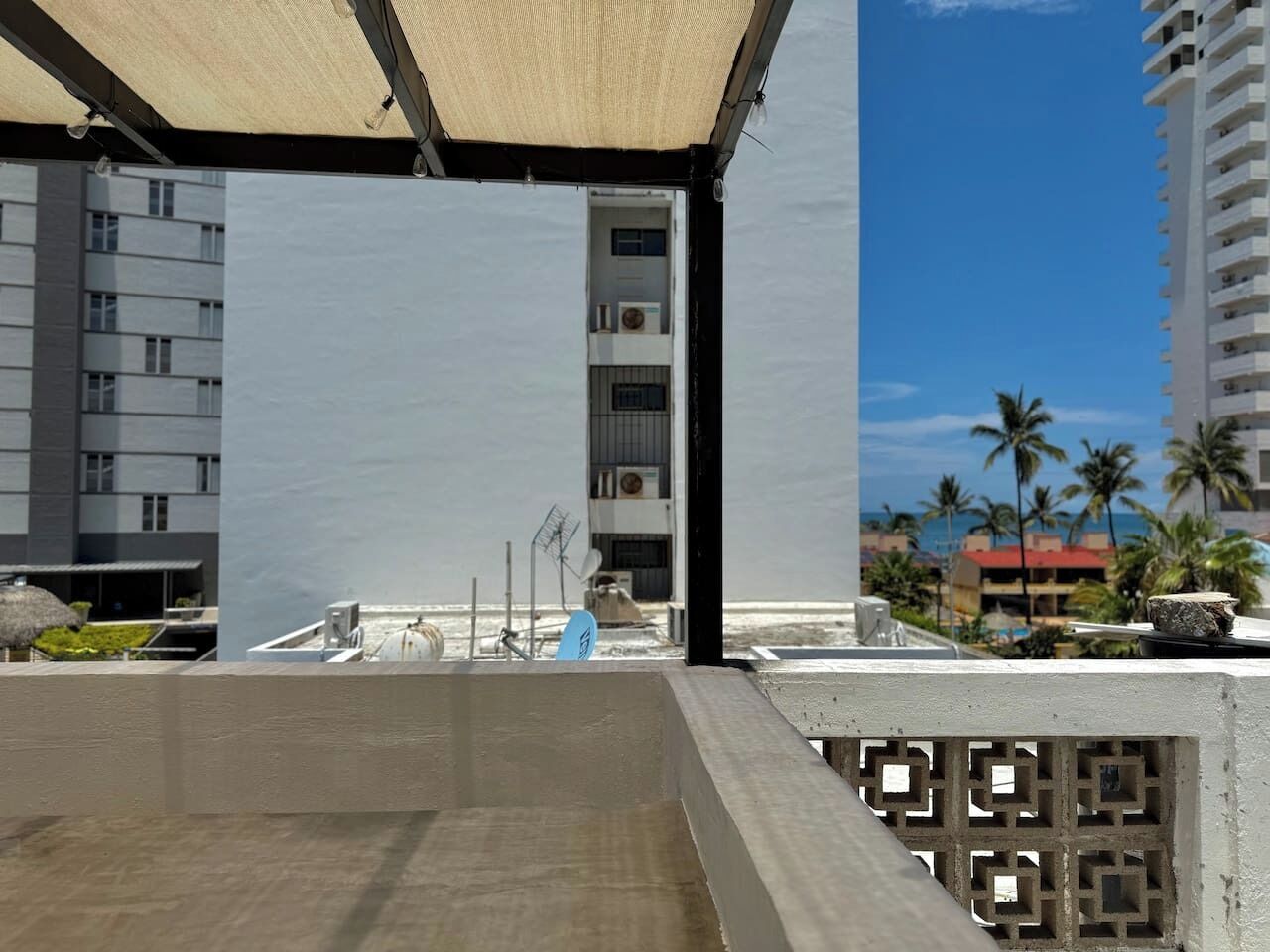 Un bâtiment moderne doté d’un toit plat, d’un balcon avec une barrière en béton et offrant une vue sur des palmiers et une plage.
