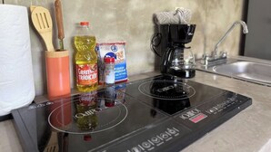 Uma cozinha com um fogão por indução preto, uma cafeteira, um frasco de óleo de cozinha, uma lata de extrato de tomate e utensílios de madeira.