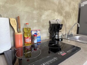 Eine Küche mit einem schwarzen Induktionskochfeld, einer Kaffeemaschine, einer Flasche Kochöl, einer Dose Tomatenmark und Holzkochlöffeln.