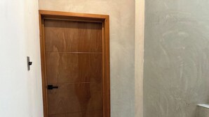 Uma porta de madeira com maçaneta preta, parede de concreto e escada com degraus brancos.