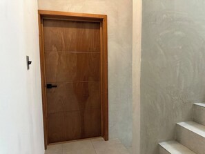 Eine Holztür mit schwarzem Griff, eine Betonwand und eine Treppe mit weißen Stufen.