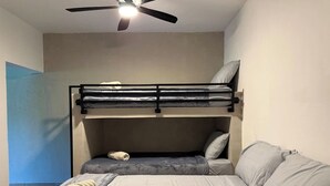 Quarto com beliches, ventilador de teto e cama com almofadas.