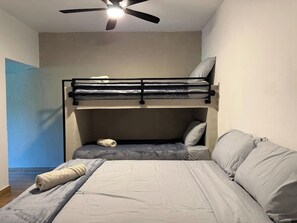 Ein Zimmer mit Etagenbetten, einem Deckenventilator und einem Bett mit Kissen.