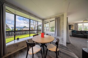 Ein Zimmer mit einem runden Holztisch und vier Stühlen, großen Fenstern mit Blick auf einen Hinterhof und einem Sofa im angrenzenden Wohnbereich.