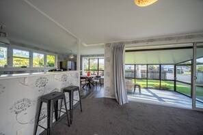 Une cuisine spacieuse avec un coin repas, de grandes fenêtres et une porte-fenêtre coulissante donnant sur un jardin.