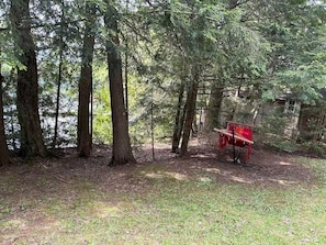 A forested area with a red bench and a small structure in the background. - Lakeside Chalet Welcomes You — Experience tranquility in nature. Pet-friendly! (Saint-Étienne-de-Bolton)