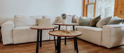 A living room with a beige sofa, two round wooden tables, and a potted plant.
