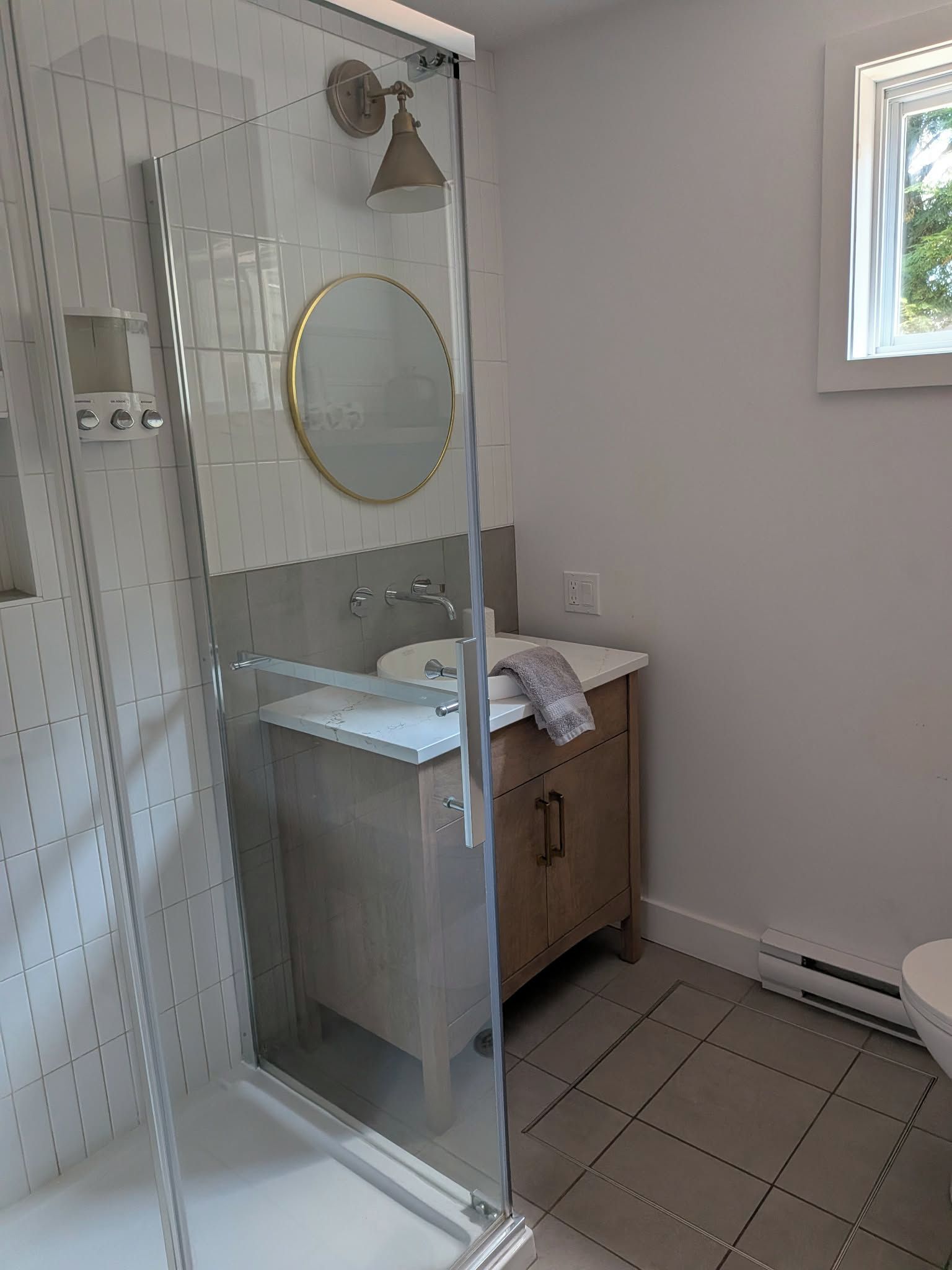 Kylpyhuone, jossa on lasiseinällä varustettu suihku, peilillä varustettu pesuallas ja wc.