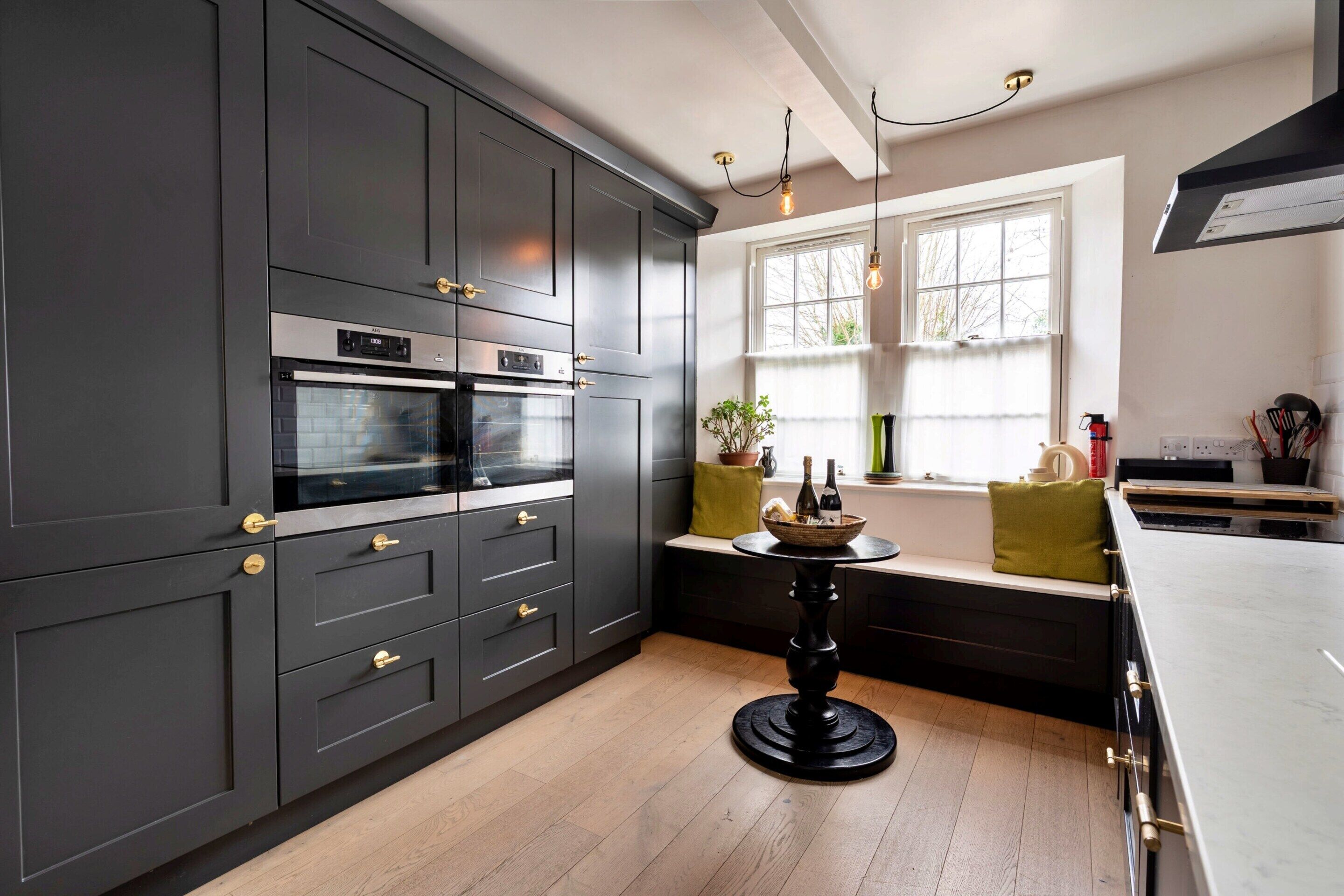 A modern kitchen with dark cabinetry, a built-in oven, and a window seat with a view.