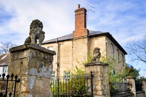 Une statue de lion en pierre se trouve devant un bâtiment doté d’une cheminée et d’une clôture en métal.