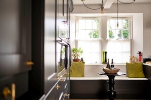 A kitchen with a window seat, a table with bottles, and a potted plant. - Heritage Holiday Home With Garden (Oxford)