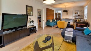 Ett modernt vardagsrum med en platt-TV, en soffa, ett soffbord och en matplats i bakgrunden.