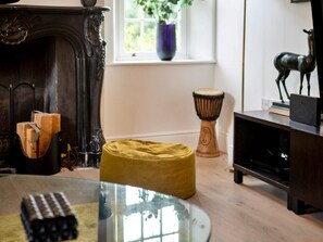 A room with a fireplace, a glass table, a yellow ottoman, a drum, and a shelf with a deer statue. - Heritage Holiday Home With Garden (Oxford)