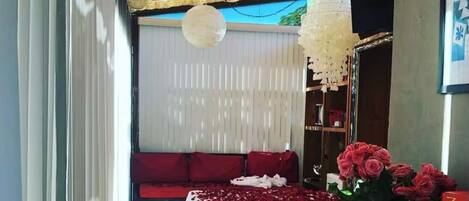 A room with a bed covered in rose petals, a chandelier, and a potted plant with red flowers.
