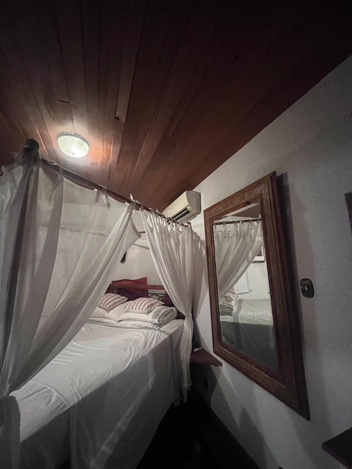 Un lit simple avec un baldaquin, un miroir au mur et un appareil de climatisation au-dessus du lit.