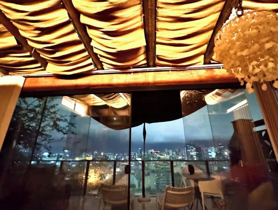 A balcony with a city view, a glass partition, and wicker furniture.
