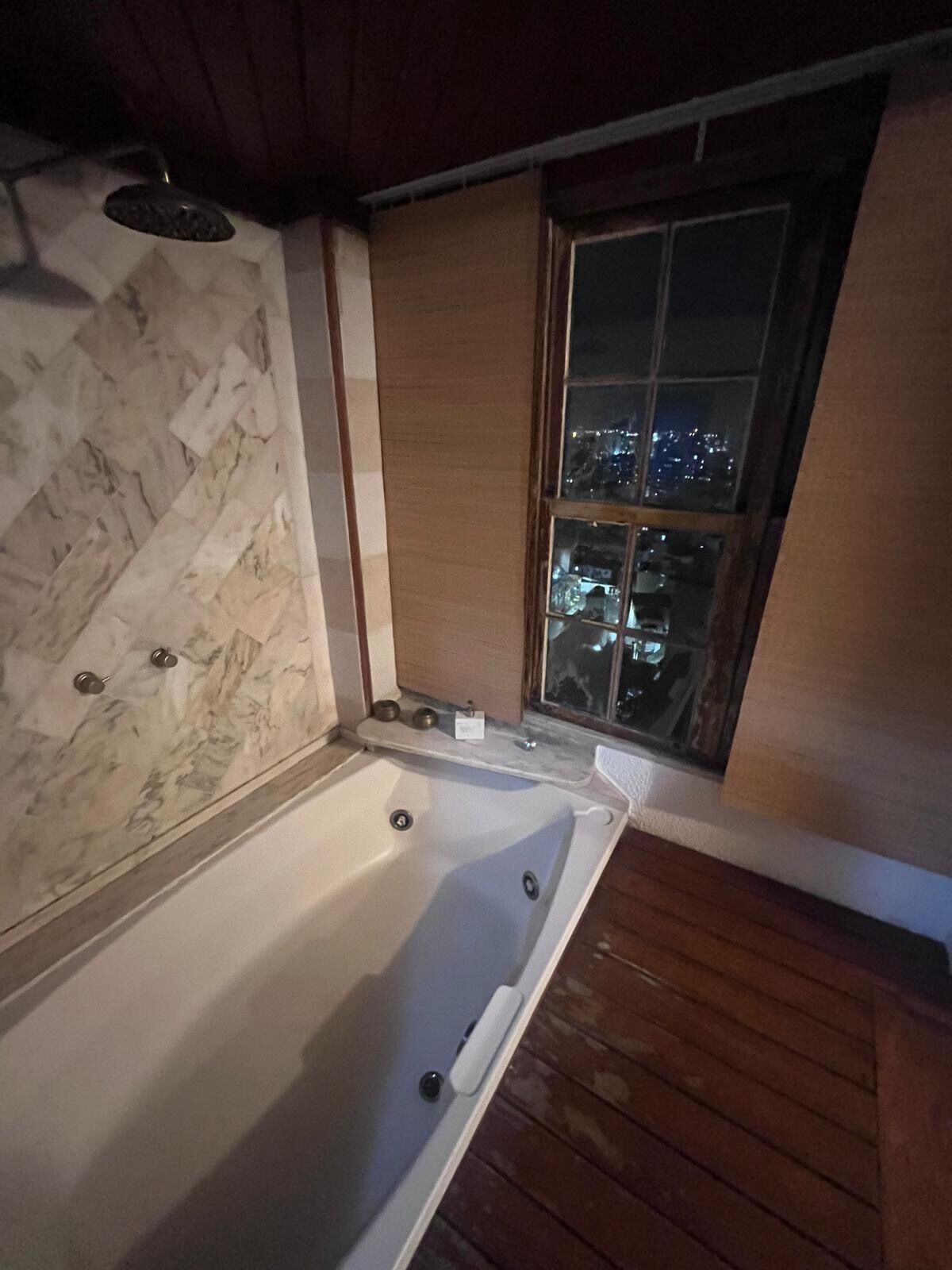 Un baño con pared de mármol, una bañera y una ventana con vista a la ciudad.