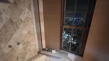 Un baño con pared de mármol, una bañera y una ventana con vista a la ciudad.