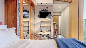 Ein Schlafzimmer mit einem Bett, einem Schreibtisch und einem Stuhl, einem an der Wand montierten Fernseher und einem Fenster.