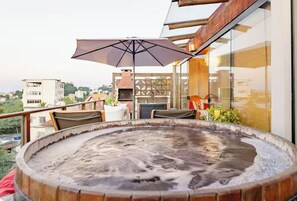 Un jacuzzi en un balcón con vistas a la ciudad, una mesa con sillas y una sombrilla.