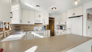 Eine moderne Küche mit weißen Schränken, einer Granit-Arbeitsplatte, einer Mikrowelle, einem Herd und einem Kühlschrank.