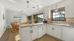 Une cuisine moderne avec des meubles blancs, un grand îlot central et un coin repas doté de chaises en bois.