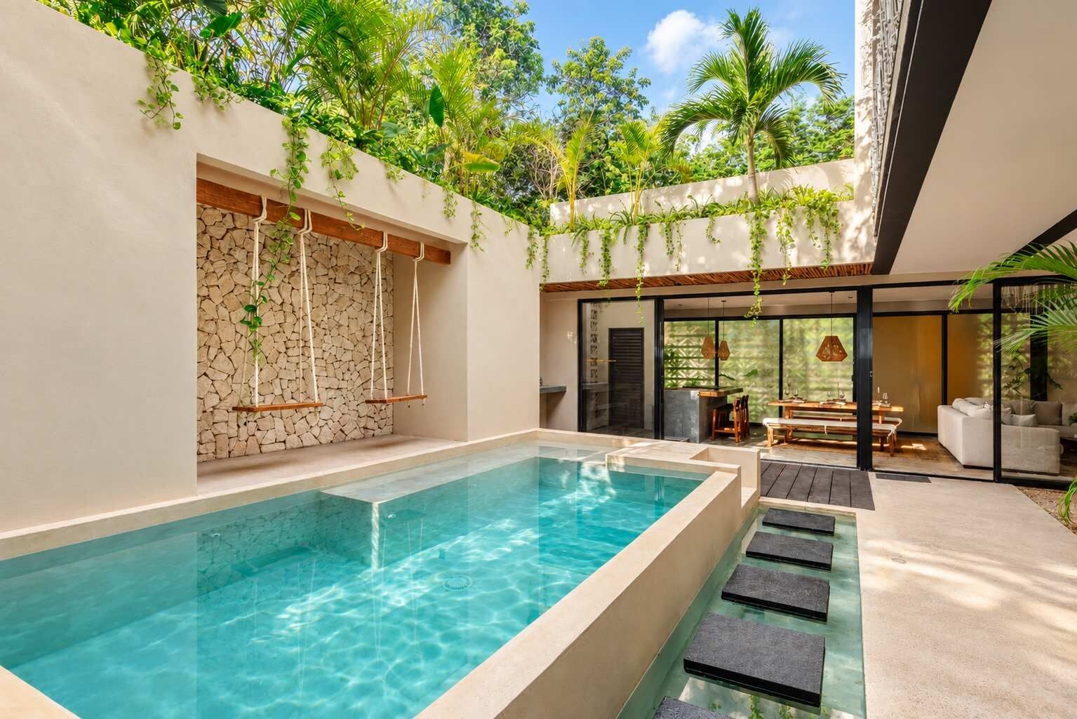 A modern outdoor pool area with a stone wall, hanging plants, and a seating area with a table and chairs.