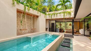 A modern outdoor pool area with a stone wall, hanging plants, and a seating area with a table and chairs.